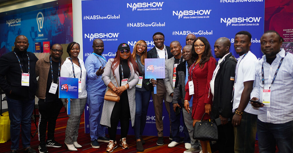 A group of international NAB Show attendees pose for a photo in front of the NAB Show Global step-and-repeat.