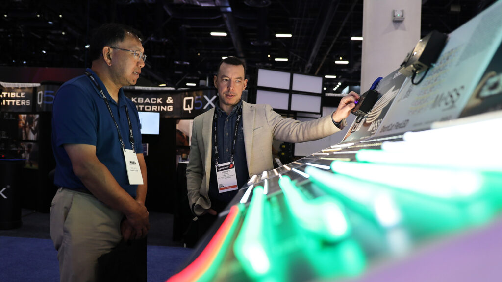 An exhibitor is showcasing new technology to an attendee at the NAB Show floor.